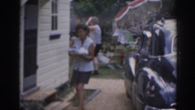1963: woman bringing leftovers in after outdoor barbecue in the back yard.
