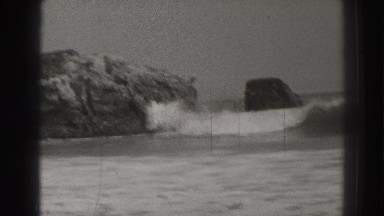 1937: children frolicking in the ocean waves that crash into beautiful rock