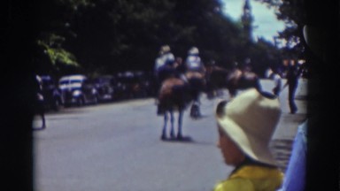 1937: several people riding horses in the street, along with one dog walking