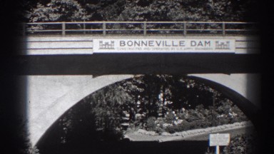 1938: drivers traverse under a bridge marking bonneville dam. BONNEVILLE