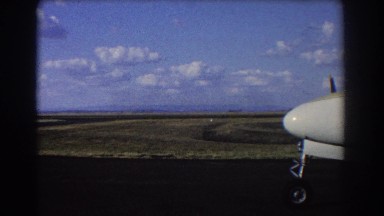 1967: nose of airplane and front wheel extend over paved runway by field