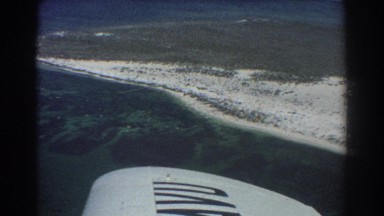 1967: a plane flies around a small sandy island in the ocean. PERTH AUSTRALIA