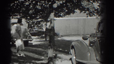 1937: a woman walks outdoors near vehicles as a car pulls away from her