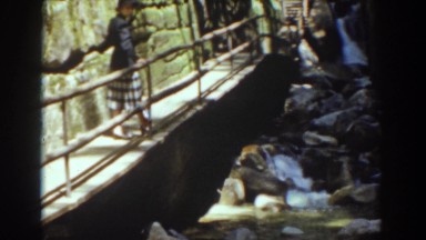 1939: woman watches little cascade standing on a bridge on a sunny day
