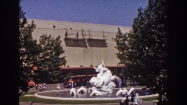 1939: a courtyard in front of a building, with a statue in a pool, with a city