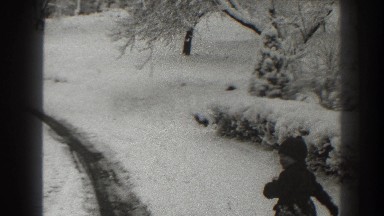 1938: child in dark outfit walks near tire track through snow-covered park