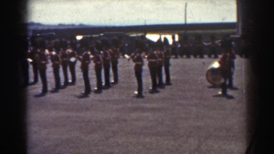 1938: a band dressed in red is marching and performing outside QUEBEC
