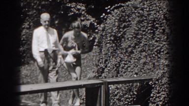1938: an aged couple walk through the orchard and the lady sits on the bench