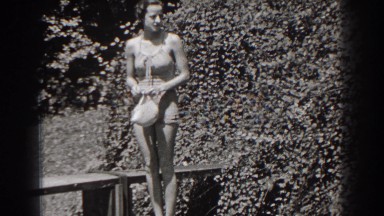 1938: woman wearing bathing suit holds swim cap then steps over railing
