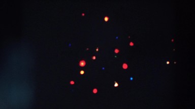 1957: a christmas tree with many hanging lights that illuminate it in the dark