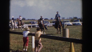 1957: some men riding on horses in the ground watched by two children WHEELING
