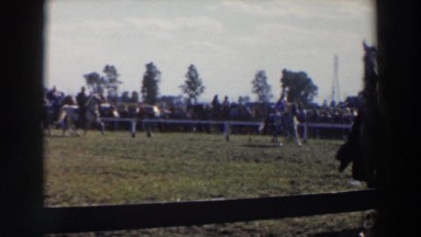 1957: people in cowboy outfits ride horses along fencing in front of spectators
