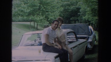 1965: husband and wife sitting on the trunk of their parked car. FALLSTON