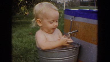 1965: Baby Girl Sitting in Bucket of Water Playing with Cap Gun