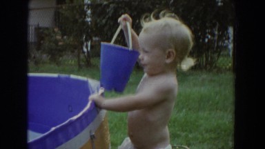 1965: a toddler sits in a metal bucket filled with water next to a swimming pool
