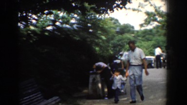 1960: a man in blue and white is walking with his son and sitting on a bench