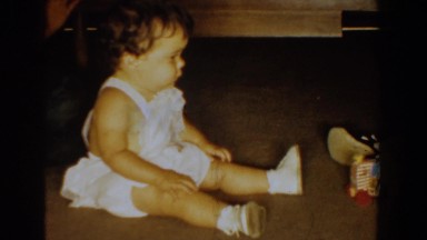 1960: a awesome baby wearing white dress sitting on the ground and playing