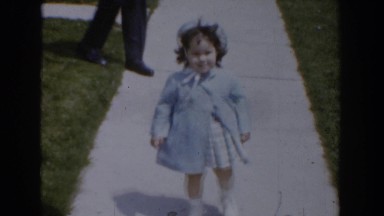 1960: a beautiful girl child with white cap is walking along the pavement