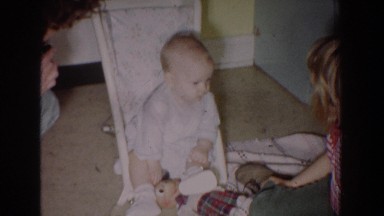 1965: baby looking at family members sitting with toys inside a room FALLSTON
