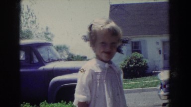 1965: a old video of a little girl in her neighborhood smiling at the camera