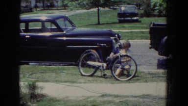 1965: a little girl rides a tricycle while her brother works on his bicycle