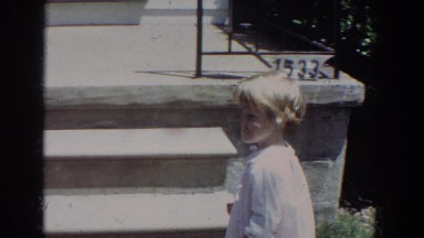 1965: small child walks up stoop opens the screen door, turns and smiles