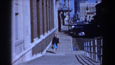 1958: a woman walking next to a large building uphill, smiling. YORKTOWN