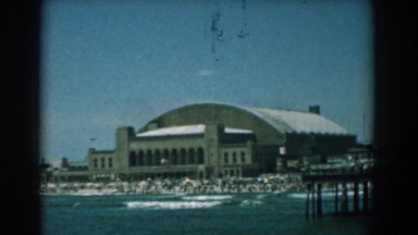 1958: a coastal city has large buildings, semicircular roofed arena