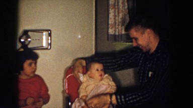 1958: A Baby Sitting in a Red Chair Wearing a Yellow Sweater and White Dress