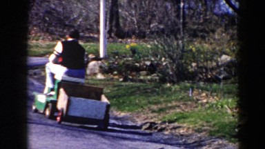 1964: Quaint Driver Straddles Lawnmower Pulling Plywood-Sided Cart in Pequot Lakes, Minnesota