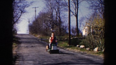 1964: Father and Son Riding Lawnmower Down Driveway, Pequot Lakes, Minnesota