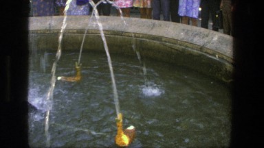 1975: group of people surrounding a man made fountain that has objects floating