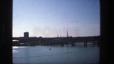 1975: view of industrial buildings over a lake, looking peaceful