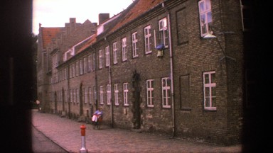 1975: panning shot of an urban town with a person walking with his/her bicycle.