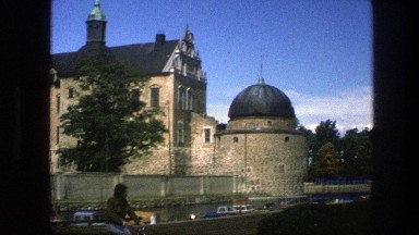 1975: buildings outside with vehicles surrounding and a person riding a bike