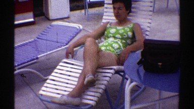 1969: Woman Wearing a Green and White Bathing Suit Relaxing by Pool