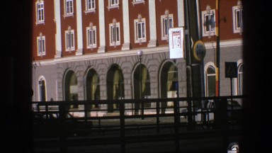 1975: cars pass on a street next to a brick building with arched windows