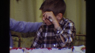 1968: two funny kids sitting at the table and one extends head towards camera