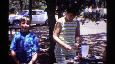 1969: preoccupied woman with two smiling boys at picnic table by parking lot