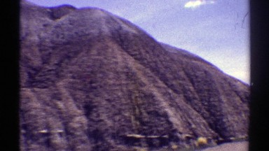 1969: a road running in the middle of a mountain with green grass and rocks