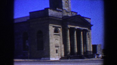 1964: survey of a structure in a town that is made of stone with vehicles going
