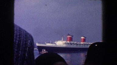 1960: people on the shore watch a cruiseliner get escorted from port