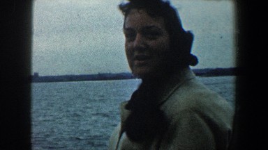 1960: a lady standing by a fence, across the river from a large city NEW YORK