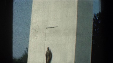 1961: a short statue in front of a tall building with large windows at the top