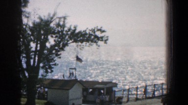 1961: Panorama Shot of Ocean and Cars Parked on Dock with People Walking