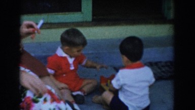 1962: woman smoking cigarette while two small boys struggle over who will play