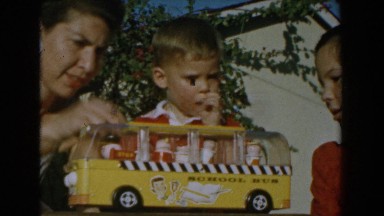 1962: mother playing with her child and his school bus toy with sibling watching