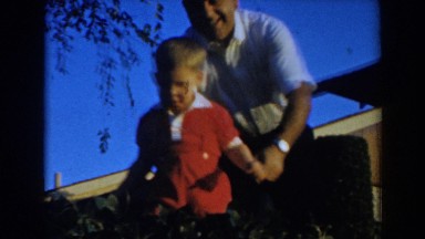1962: a toddler boy walks carefully through a garden with foliage and bushes