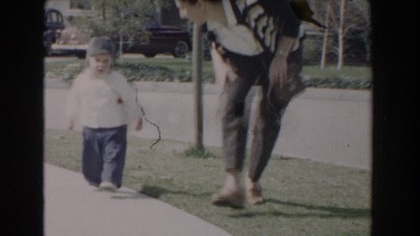 1962: mom helps her baby to walk along the pavement himself in the park