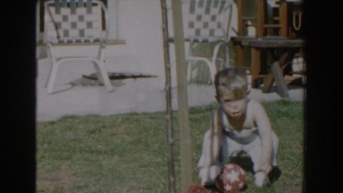 1962: little boy picking up a toy ball out in the yard. GLENDALE, CALIFORNIA